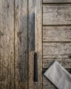 Hand forged cleaver with dark cord wrapped handle standing upright edge on against weathered boards, canvas roll below