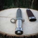 Hand forged Damascus bayonet dagger with fluted steel grip, top down view from the pommel with its sheath alongside on wood