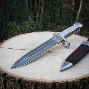 Hand forged damascus bayonet knife with a fluted polished steel grip, ring guard and triskele engraving lying on a pale wood stump beside its brown leather sheath