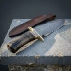 Hand forged Damascus bowie knife with ram horn handle, view from the handle end over the brass guard and patterned blade
