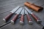 Hand forged Damascus chef knife set with rosewood handles, handle end view of five knives fanned on decking with the leather roll