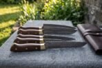 Hand forged Damascus chef knife set with walnut handles and brass bolsters, handle end view of five blades stacked on stone