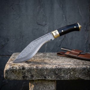 Hand forged Damascus kukri with black horn handle, side view at the edge of a stone bench against a dark slate wall