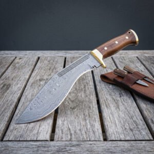 Hand forged Damascus kukri blade with brass bolster shown point down on wooden decking, companion knives in the sheath