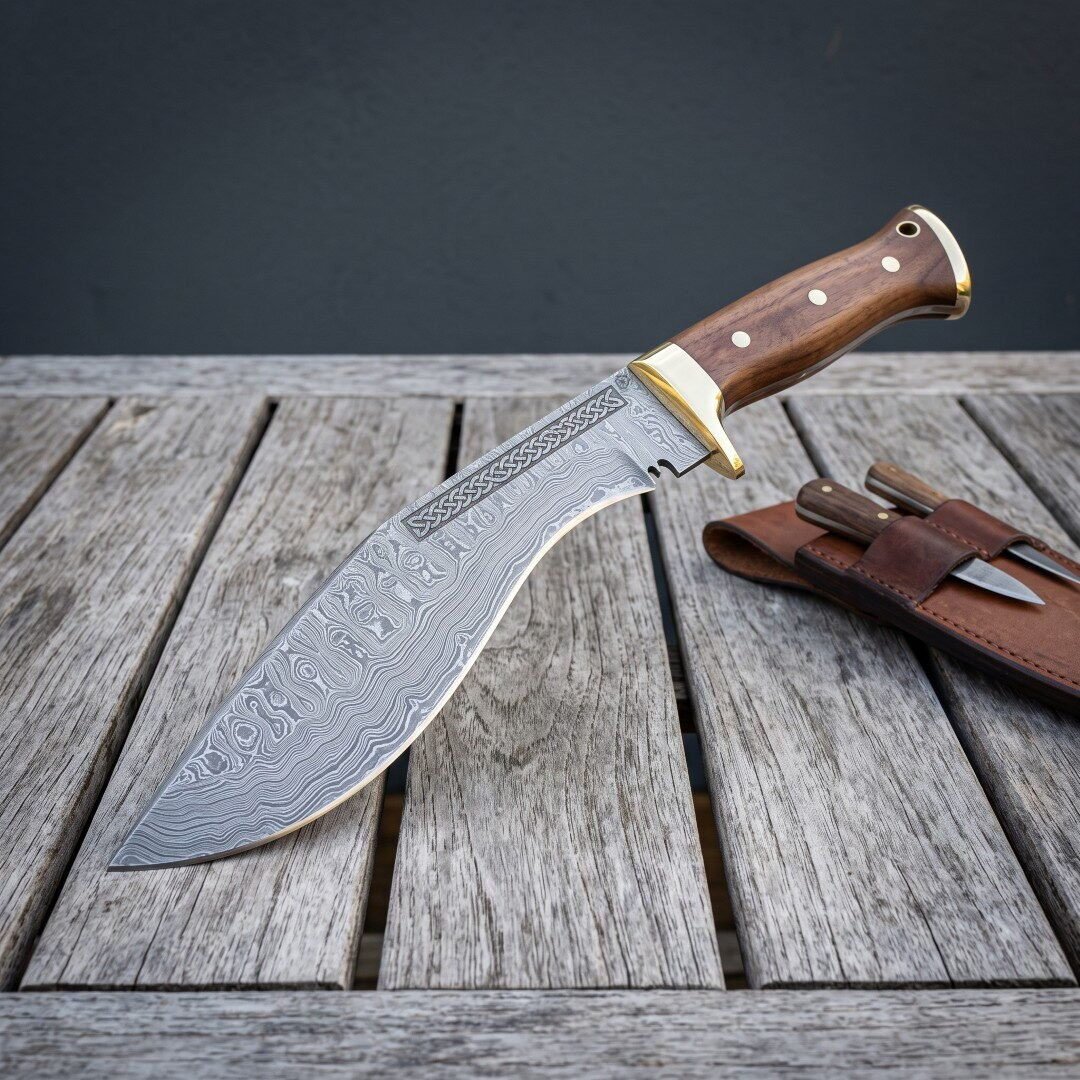 Hand forged Damascus kukri blade with brass bolster shown point down on wooden decking, companion knives in the sheath Hand forged Damascus kukri blade with brass bolster shown point down on wooden decking, companion knives in the sheath