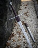 Hand forged flame bladed longsword with leather wrapped grip leaning on a stone wall at an angle beside its matching dagger