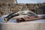 Hand forged kukri with buffalo horn handle and brass fittings resting on a stone trough beside its leather sheath
