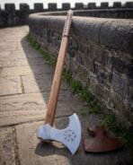 Hand forged long handled Viking axe with bearded head and etched Vegvisir, low close view leaning on a stone parapet