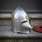 Hand forged medieval helmet in the pig faced bascinet pattern, satin 18 gauge steel with a hinged hounskull visor and brass mounts, on grey stone steps