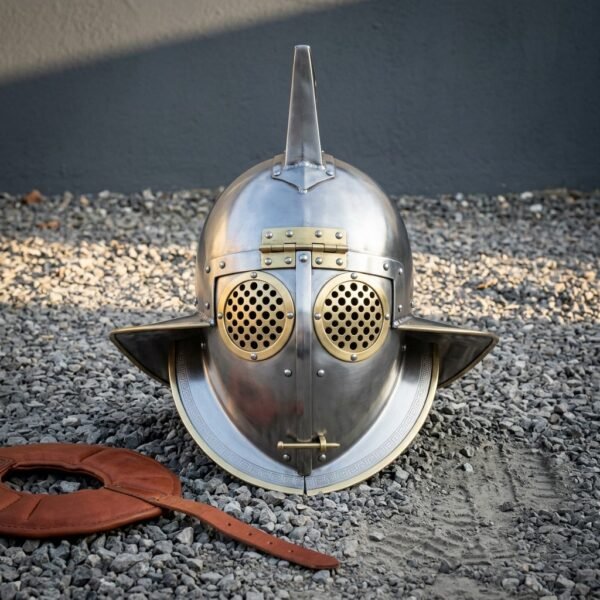 Hand forged roman helmet in the murmillo gladiator pattern, 18 gauge steel with brass rimmed perforated eye discs, crest fin and wide neck guard, on grey gravel