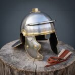 Hand forged roman helmet of Imperial Gallic pattern in brushed steel with brass meander brow band, hinged cheek guards and crest holder, set on a wooden stump