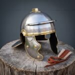 Hand forged roman helmet of Imperial Gallic pattern in brushed steel with brass meander brow band, hinged cheek guards and crest holder, set on a wooden stump