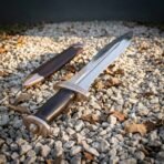 Hand forged Roman pugio dagger with raised midrib blade and bronze guard lying on gravel and autumn leaves beside its sheath