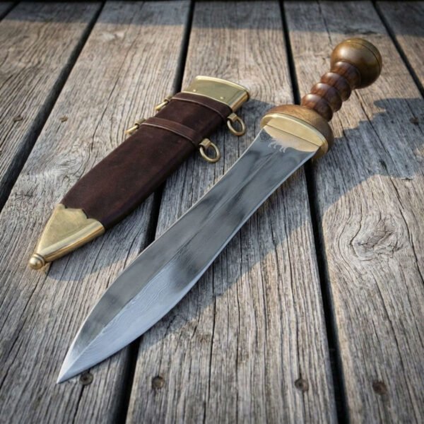 Hand forged Roman pugio dagger with waisted blade and ribbed hardwood grip, diagonal view on decking with its leather sheath