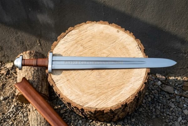 Hand forged rune engraved sword with Elder Futhark inscription cut into the fuller, russet leather grip and domed steel pommel lying on an oak log round