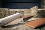 Hand forged stainless steel kitchen cleaver with cord wrapped handle and engraved knotwork panel shown close on a stone step
