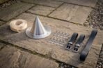 Hand forged steel conical Viking shield boss with rivets, black leather straps and a rolled leather strip, angled view on garden paving