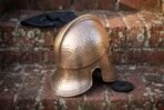 Hand forged steel Corinthian Greek helmet with hammered bronze tone crown, rear three quarter view on brick steps