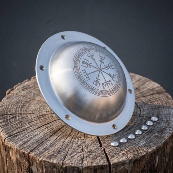 Hand forged steel shield boss with Vegvisir engraved dome and rivet flange, angled on a tree stump with rivets in a row