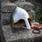 Hand forged steel Viking conical nasal helmet with brass rivets and valknut engraving, angled view on stone with a leather pouch