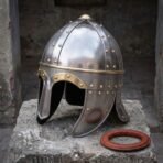 Hand forged steel Viking spectacle helmet with brass brow band and riveted eye guards, angled view on stone by its liner ring