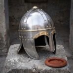 Hand forged steel Viking spectacle helmet with riveted skull and brass brow band on a stone block beside the leather liner ring