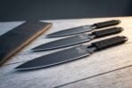 Hand forged throwing knives with cord wrapped handles, low view of three black blades fanned on wooden planks beside the roll