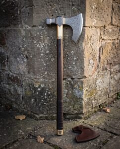 Hand forged Viking bearded axe with etched knotwork head, engraved brass collar and leather wrapped haft leaning against a lichen covered sandstone wall