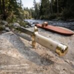 Hand forged Viking Bowie knife with bone handle and brass guard, angled view on a river boulder with its leather belt sheath