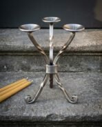 Hand forged viking candle holder in twisted brushed steel with three pricket branches, Mjolnir engraved collar and scrolled feet, on a stone step beside beeswax tapers