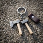 Hand forged viking keyring with miniature damascus axe and hammer charms on ash handles and a brown leather fob lying on wet gravel