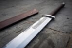 Hand forged Viking langseax with leather wrapped grip, close view of the knotwork etched blade on stone paving with scabbard