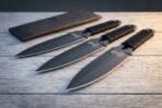 Hand forged Viking throwing knife set with black blades and cord wrapped handles, angled on a wooden table with leather roll sheath