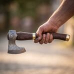 Hand holding a Damascus bearded axe with etched wolf head, walnut haft and brass fittings against a blurred street