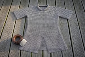 Hand made chainmail hauberk in butted mild steel rings laid flat on decking, thigh length with short sleeves, a standing collar and a split skirt.