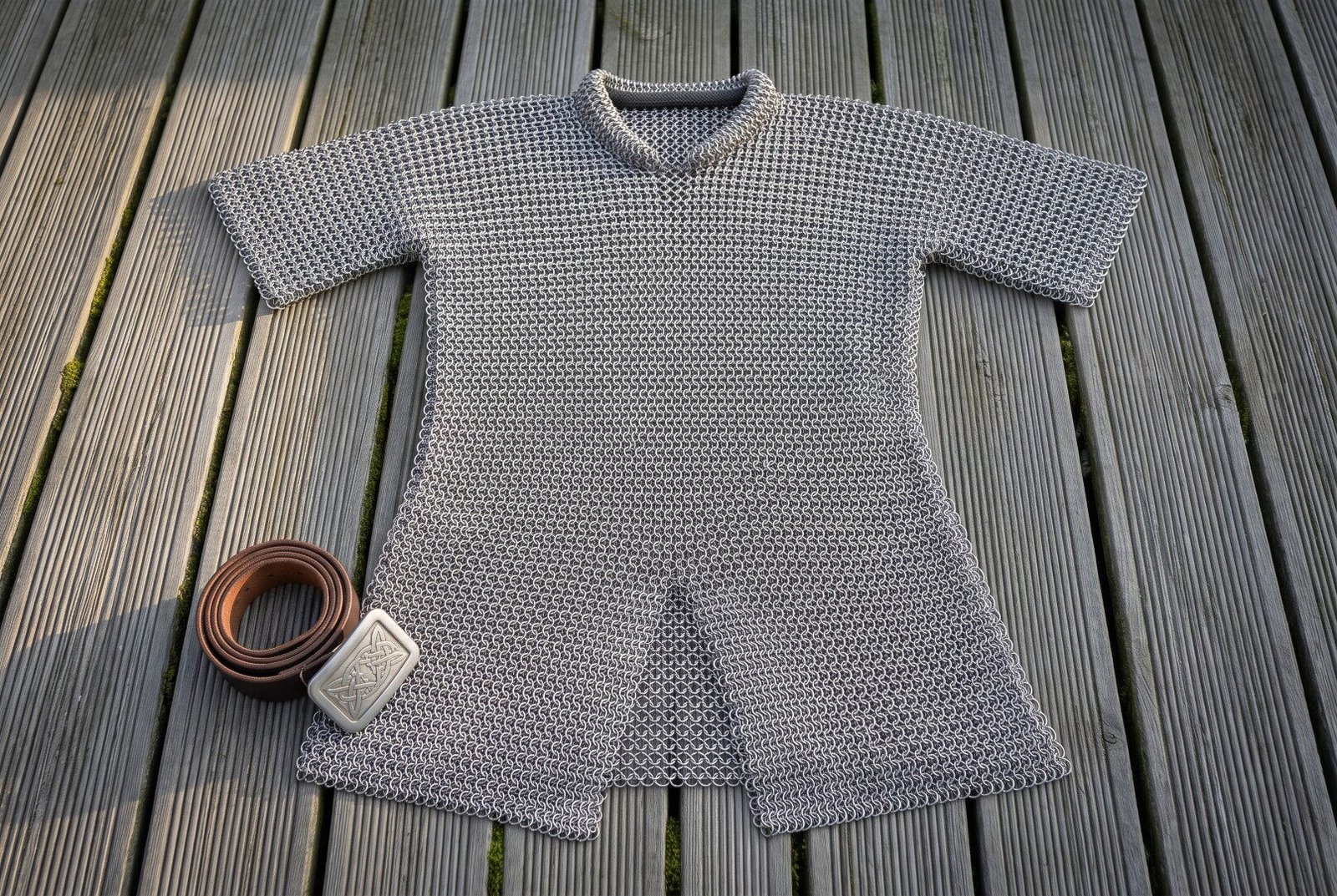Hand made chainmail hauberk in butted mild steel rings laid flat on decking, thigh length with short sleeves, a standing Hand made chainmail hauberk in butted mild steel rings laid flat on decking, thigh length with short sleeves, a standing collar and a split skirt.