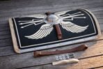 Hand made curved Roman scutum shield with black face, painted wings and rawhide edge laid flat on planks with straps and rivets