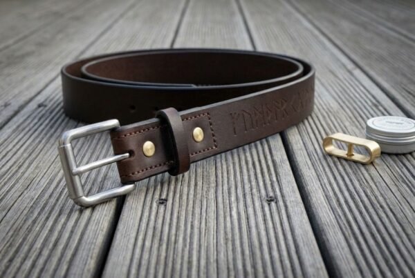 Hand made dark brown full grain leather rune belt with brass rivet, rolled into a coil on grey decking, buckle facing forward