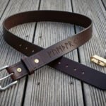 Hand made dark brown leather rune belt with stamped Elder Futhark line, looped on decking with brass fittings and a tin of balm