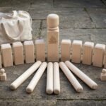 Hand made kubb set in pale maple laid out on stone paving with a Valknut engraved king, ten kubb blocks, six throwing batons and a canvas carry bag
