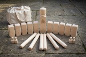 Hand made kubb set in pale maple laid out on stone paving with a Valknut engraved king, ten kubb blocks, six throwing batons and a canvas carry bag