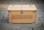 Hand made oak Viking storage chest with carved knotwork front panel and steel strap hinges, front view on stone paving