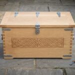 Hand made oak Viking storage chest with carved knotwork front panel and steel strap hinges, front view on stone paving