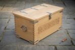 Hand made oak Viking storage chest with dovetailed corners and lockable hasp, three quarter view showing the side ring handle on paving