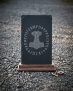 Hand made runic slate plaque engraved with a knotwork Mjolnir inside a full Elder Futhark rune ring, standing in a solid walnut base on grey pebbles.