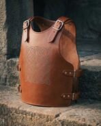 Hand made tan leather medieval cuirass with Celtic knotwork chest panel and buckled shoulders, angled view on stone steps