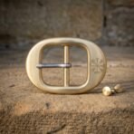 Hand made viking belt buckle in brushed solid brass with an engraved Vegvisir stave and a steel tongue, sitting on a sunlit sandstone ledge beside two brass screw studs