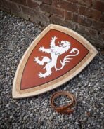 Hand made wooden heater shield painted with a white rampant lion on red, lying on gravel beside its leather arm strap