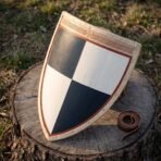 Hand made wooden heater shield quartered in navy and white with rawhide edge, angled on a tree stump beside its leather strap