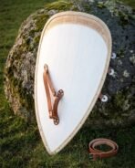 Hand made wooden Templar kite shield back view with leather grip and rawhide bound edge, leaning on a mossy boulder in grass